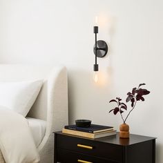 a nightstand with books and a potted plant on it next to a white bed