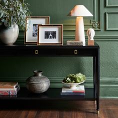 a black table topped with pictures and a lamp next to a potted plant on top of a wooden floor