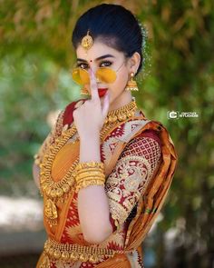 a woman dressed in an orange and gold sari holding a glass with her nose