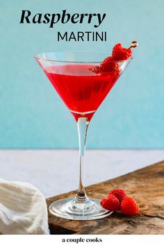 a red drink in a martini glass with raspberries on the rim next to it