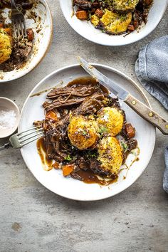 two plates filled with meat and vegetables covered in gravy next to silverware