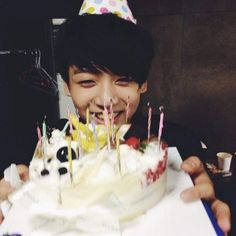 a young boy smiles as he holds up a birthday cake with lit candles on it