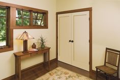 a room with a table, chair and lamp in it next to a door that leads to another room