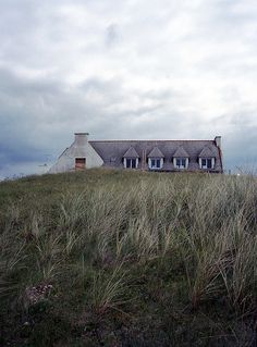 a large house sitting on top of a lush green hillside next to a tall grass covered hill