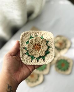 a hand holding a small crocheted square with a flower in the center and green leaves on it