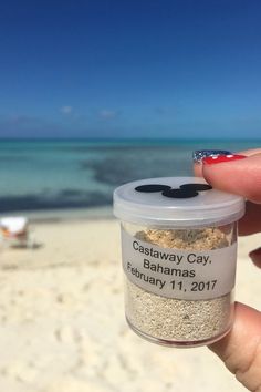 someone is holding up a jar of sand on the beach