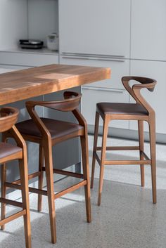 a wooden table with four chairs around it in a modern kitchen, next to an island