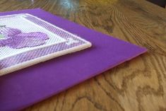 a purple place mat sitting on top of a wooden table next to a vase filled with flowers