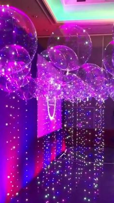 purple and white balloons floating in the air with lights all around them at a party