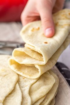 a stack of tortillas sitting on top of a table next to a person's hand