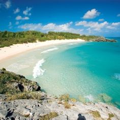 an aerial view of a sandy beach and turquoise water with green trees in the background