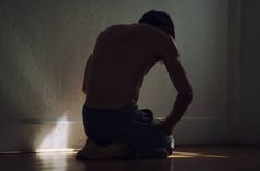 a shirtless man sitting on the floor in front of a wall with his hands behind his back