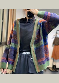 a woman taking a selfie in front of a mirror wearing a colorful cardigan