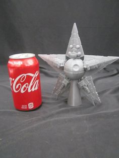 a coca - cola can sitting next to a model star wars fighter jet on a table