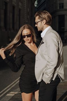 a man and woman standing next to each other on the street in front of buildings