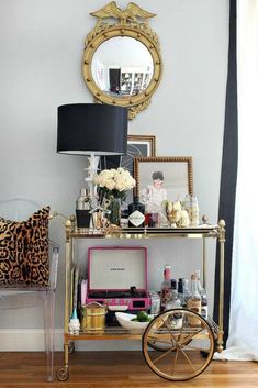 a gold bar cart filled with liquor bottles and other items in front of a mirror