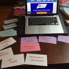 an open laptop computer sitting on top of a wooden desk covered in sticky notes and post - it notes