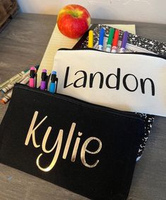 two personalized pencil cases sitting on top of a table next to an apple and crayons