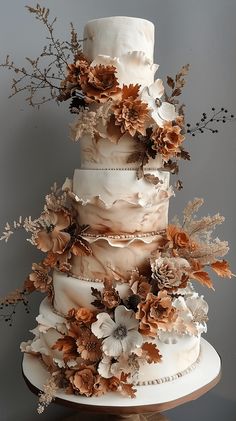 a three tiered cake decorated with flowers and leaves on a table next to a wall