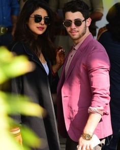 a man and woman standing next to each other in front of a crowd wearing sunglasses