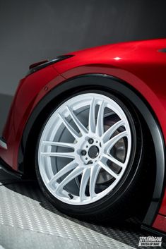 a red sports car with white spokes is parked in a parking lot and it's wheels are visible