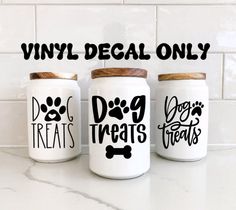 three jars with dog treats on them are sitting on the counter next to a tile wall