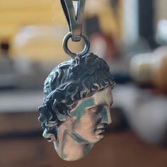 a close up of a silver necklace with a statue on it's face hanging from a chain