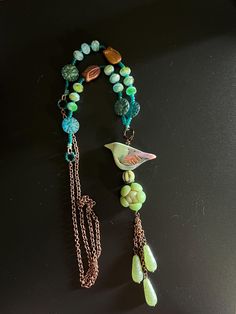 This nature inspired necklace features a 2x1" green clay bird with flowers and leaves handmade by Heather Powers perched on a teal, green and gold melon bead and bead cap, 1" green drop beads, 1" green clay cactus flower, blue and green pressed glass beads, teal seed beads copper colored tulip beads, and gorgeous multi color glass beads, all strung on Irish waxed linen, all attached to copper chain.  The pendant portion is approximately 5 1/2" long, and the entire rope chain portion is 29" long.  The drop is 14 1/2". Clay Cactus, Tulip Beads, Bird With Flowers, Clay Bird, Beach Jewelry Boho, Green Clay, Polymer Crafts, Inspired Necklace, Flower Blue