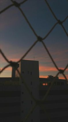 an airplane is flying in the sky behind a chain link fence with buildings in the background