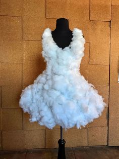 a mannequin is covered in white fluffy clouds on a black stand next to a brick wall