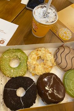 a box filled with different types of donuts next to a cup of coffee on a table