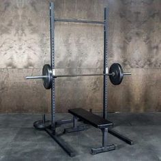 a squat bench and barbell rack in front of a wall with concrete flooring