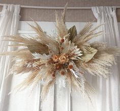 an arrangement of dried flowers and leaves on a window sill in front of curtains