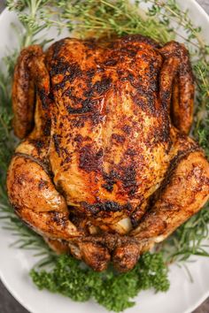 a roasted chicken on a white plate with fresh herbs