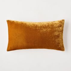 an orange velvet pillow sitting on top of a white wall