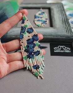 a hand holding a beaded necklace in front of a picture frame with other beads