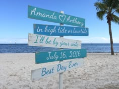 a wooden sign sitting on top of a sandy beach next to the ocean and palm trees