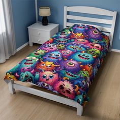 a bed with colorful monsters on it in a blue room next to a white night stand