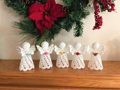 four crocheted angel figurines sitting on top of a wooden table next to a christmas wreath