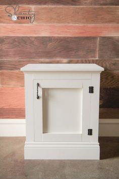 a small white cabinet sitting on top of a floor next to a wall with wooden planks