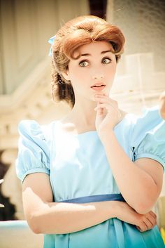 a woman in a blue dress with her hands on her chin looking at the camera