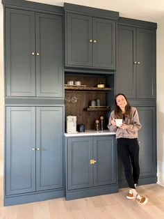 a woman sitting on the kitchen counter in front of some cupboards holding a cup