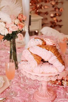 a pink table topped with lots of pastries and flowers next to a vase filled with roses