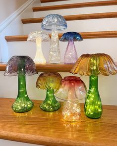 four different colored glass lamps sitting on top of a wooden table next to some stairs