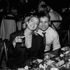 a man and woman sitting next to each other at a table with wine glasses in front of them