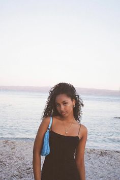 a woman in a black dress standing on the beach