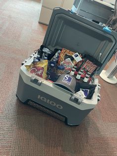 an open cooler filled with drinks and snacks on top of a carpeted floor in a room