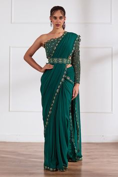 Bottle green pre-draped saree with pleated drapes, attached draped pallu and floral cut work embroidered border. Paired with one shoulder neck padded blouse with all over tonal cut dana, sequin, pearl embroidery and belt.
Components: 3
Pattern: Embellished
Type Of Work: Pearl, Sequin and Cut Dana Work
Neckline: One Shoulder Neck
Sleeve Type: One Side Full Sleeve
Fabric: Georgette, Opada Silk, Net, Organza, Lining: Shantoon
Color: Green
Other Details: 
Floral cut work hem
Embroidered belt
Attache Braidsmaid Dresses, Saree With Belt, Draped Saree, Sari Design, Fancy Sarees Party Wear, Sari Dress, Simple Sarees, Drape Saree, Indian Bridal Dress