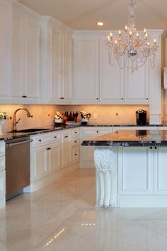 a large kitchen with marble counter tops and white cabinets, chandelier hanging from the ceiling