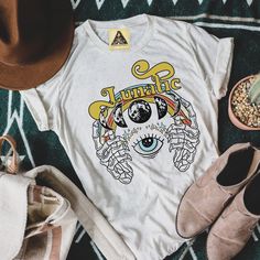 "LUNATIC (UNISEX TEE) Designed and handmade in Phoenix. The best kind of lunatic. Hey, Moon Child! This gorgeous, hand-drawn, mystical tee has all of your favorite things: skeleton hands, a retro rainbow, an evil eye, moon phases, and a hand-drawn vintage font. Grab the matching kids or baby tee/bodysuit for the perfect Mommy and Me set! ★ABOUT OUR UNISEX TEES★ Our unisex tees are super soft, long and lean. Customers consistently mention the tees run large, so order down for a tighter fit. Our c Graphic Tee With Moon Print For Festival, Casual Moon Print Tops For Festival, Cotton Tops With Moon Print For Festival, Festival Graphic Tee With Moon Print, Skeleton Hands Shirt, Moon Phases Shirt, Vintage Font, Moon Shirt, Retro Rainbow